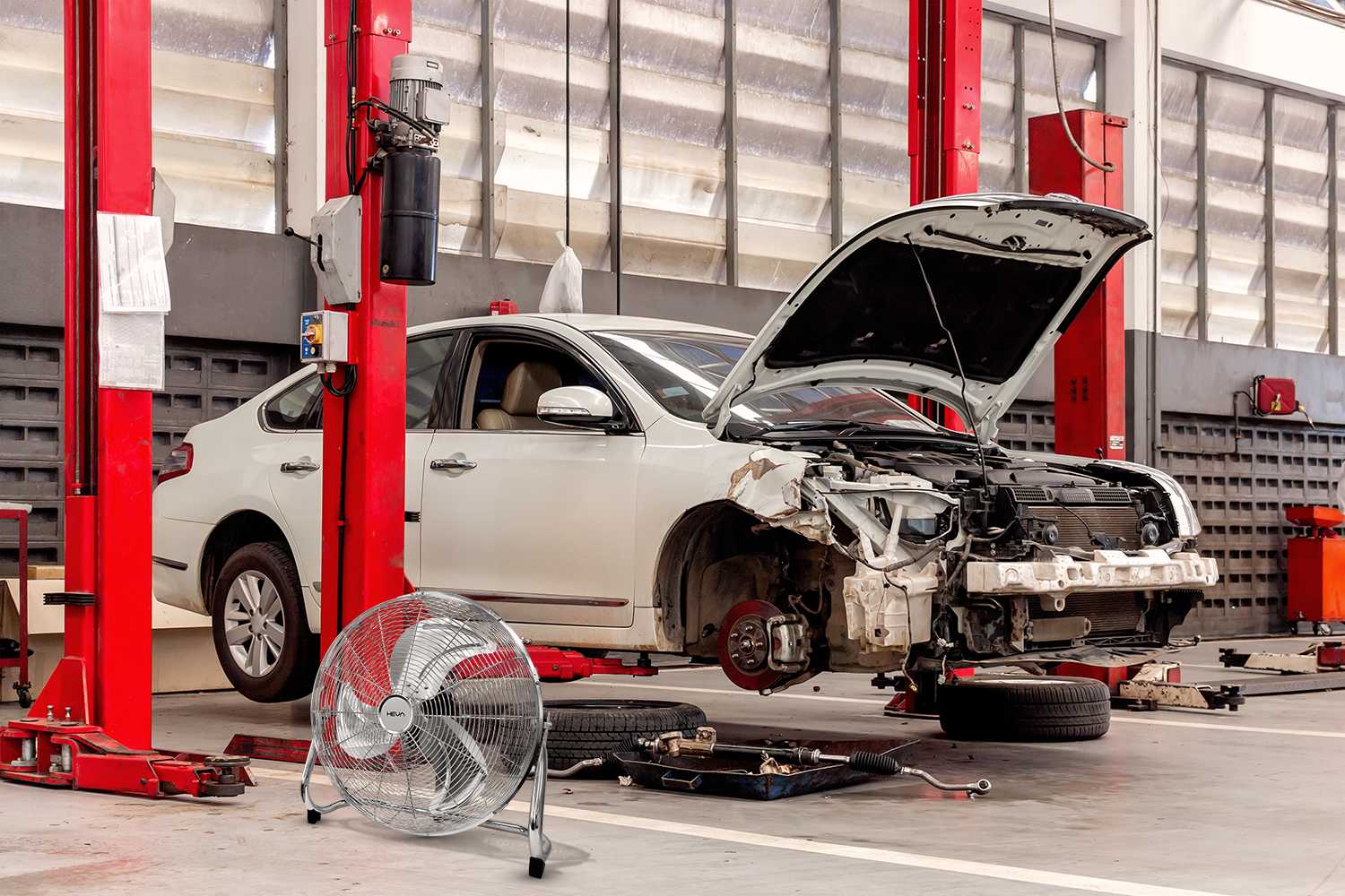 Biały samochód jest naprawiany w warsztacie, na podnośniku. Komora silnika jest otwarta.