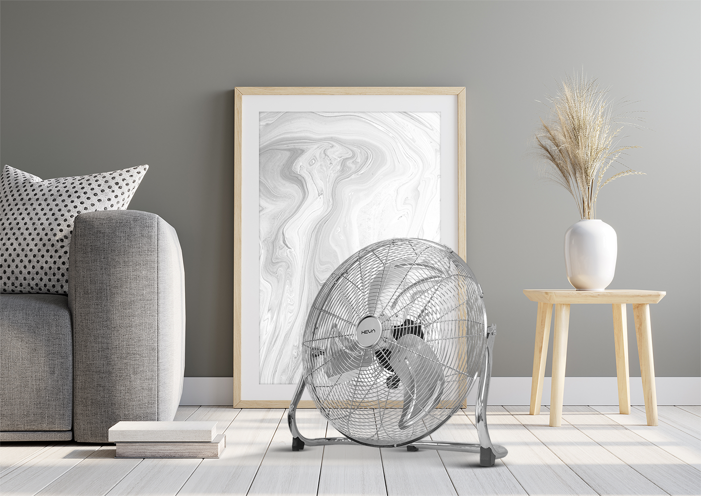 Chromowany wentylator stoi na drewnianej podłodze przed oprawionym abstrakcyjnym dziełem sztuki.