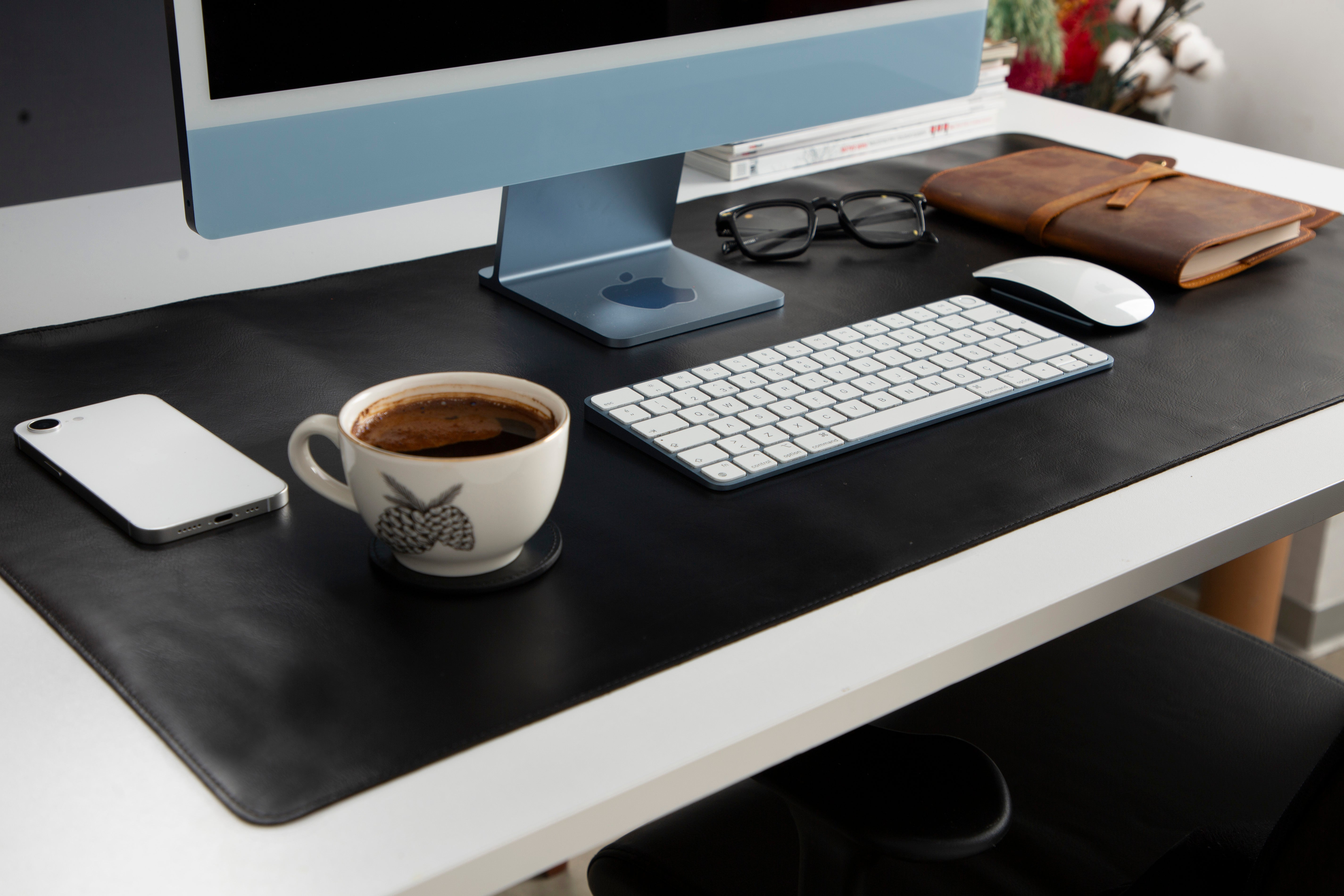 Mavi iMac, klavye, fare, defter, gözlük ve kahve bulunan bir masa.