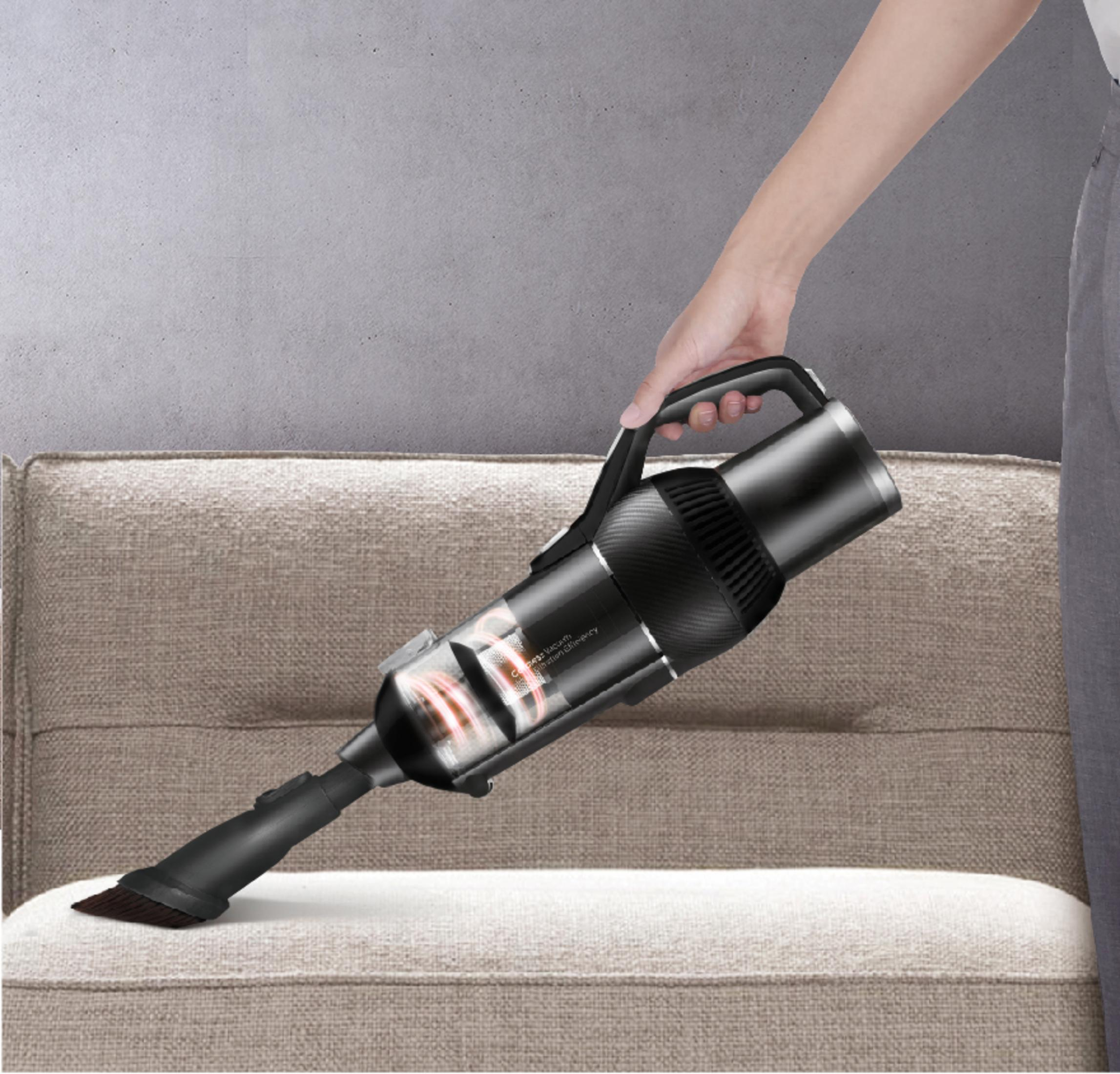 Person saugt Sofa mit schwarzem Handstaubsauger