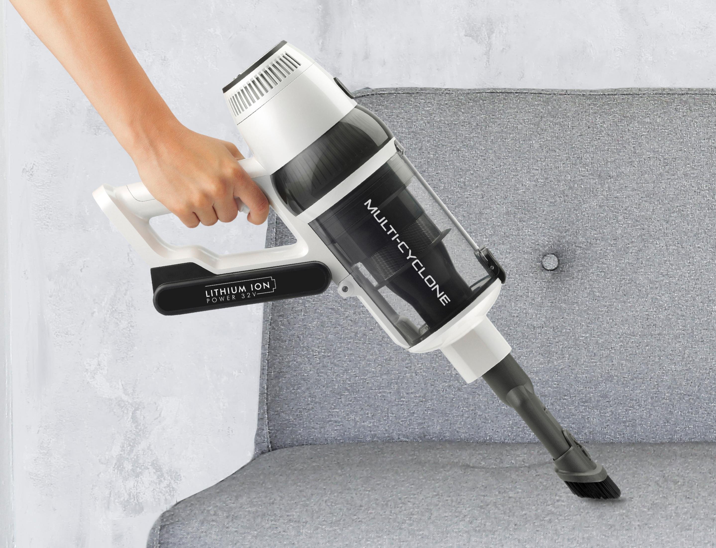 Eine Hand hält einen weißen Akku-Staubsauger über einem grauen Sofa.