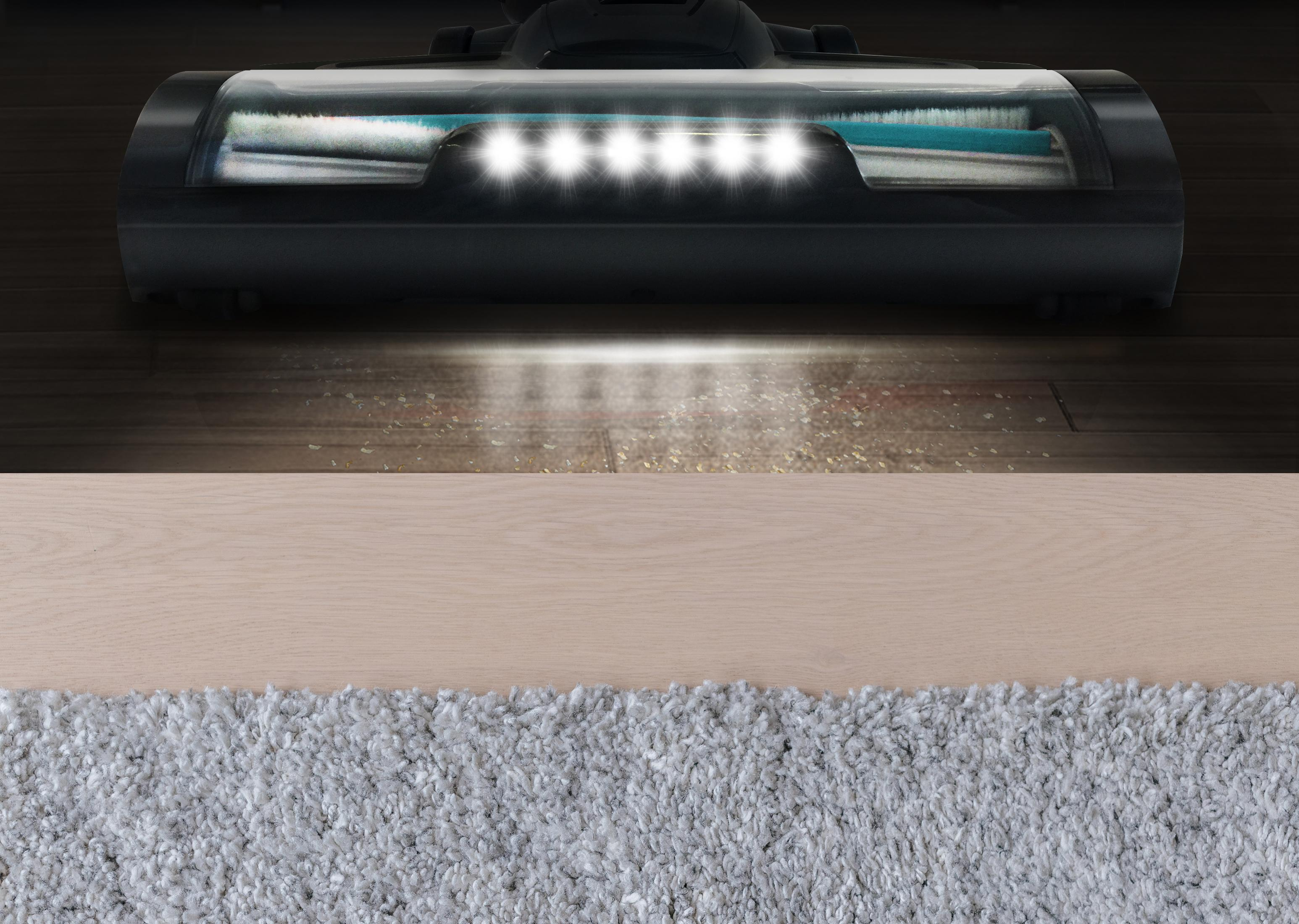 Una testina dell'aspirapolvere pulisce un pavimento in legno e un tappeto con luci.