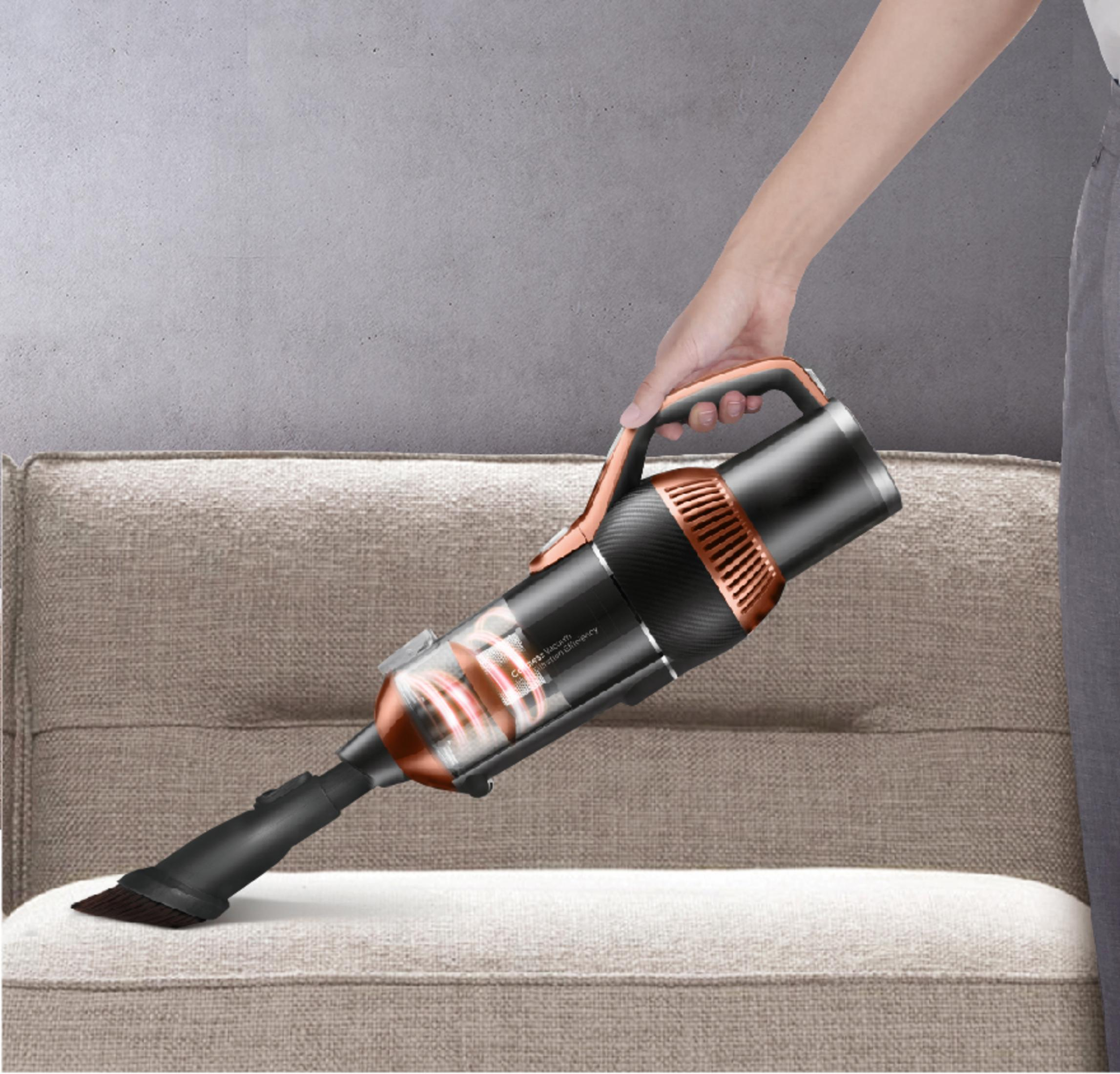 Eine Hand hält einen schwarzen und kupferfarbenen Staubsauger über einem beigefarbenen Sofa.
