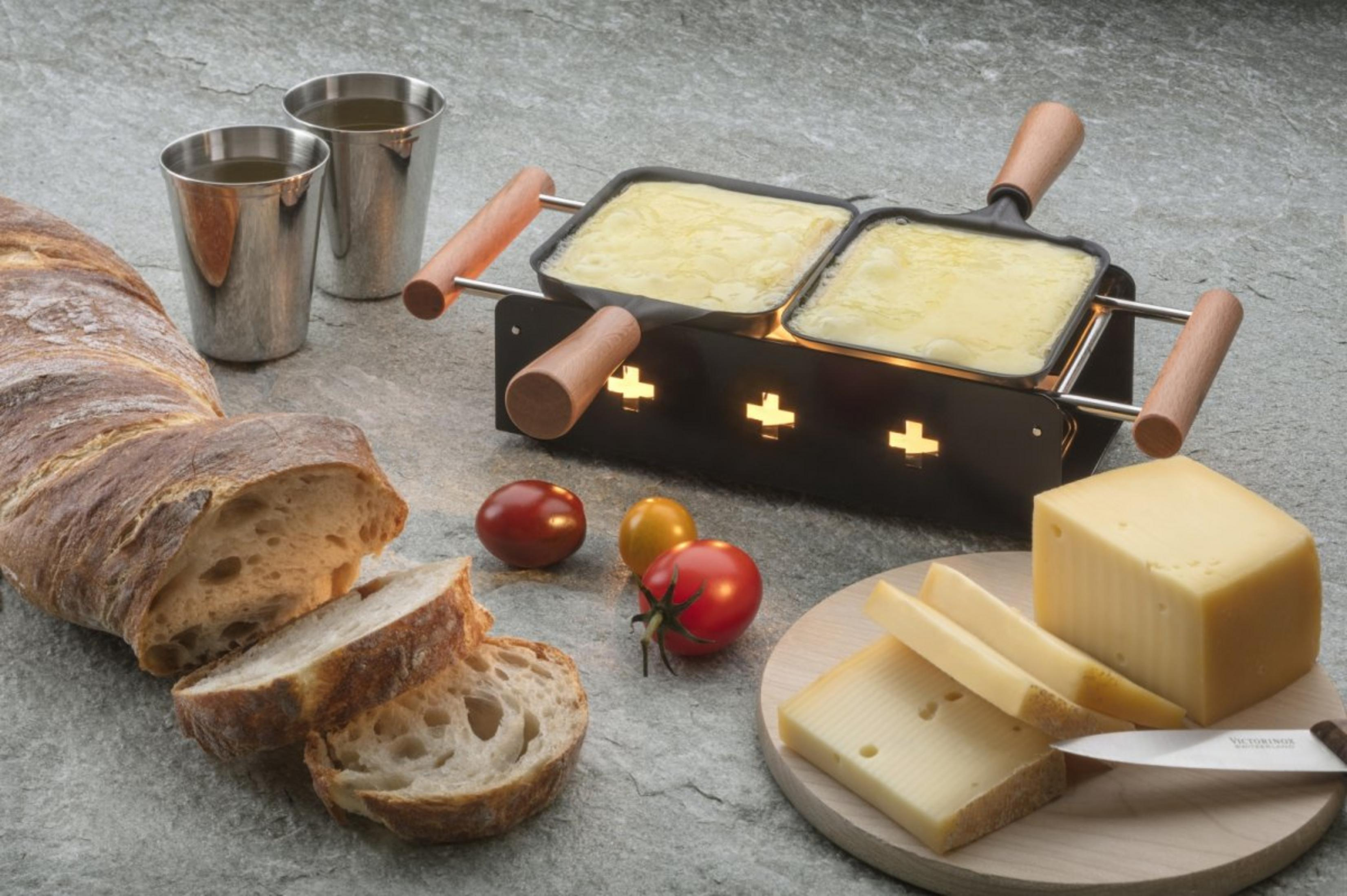 Grill per raclette con formaggio, pane, pomodori e due bicchieri.