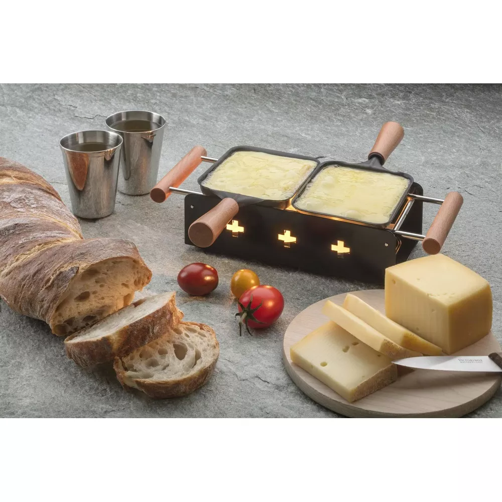Grill per raclette con formaggio fuso, pane, pomodori e formaggio su tagliere.
