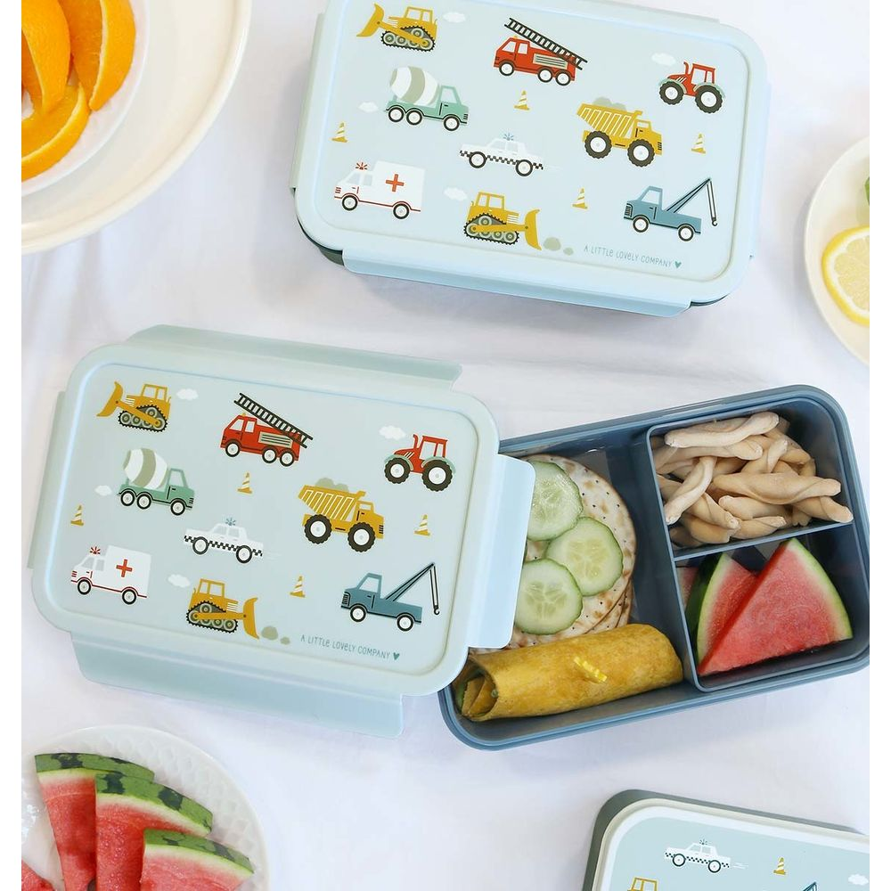 Un lunchbox aperto con cibo, accanto un lunchbox chiuso con veicoli da cantiere.