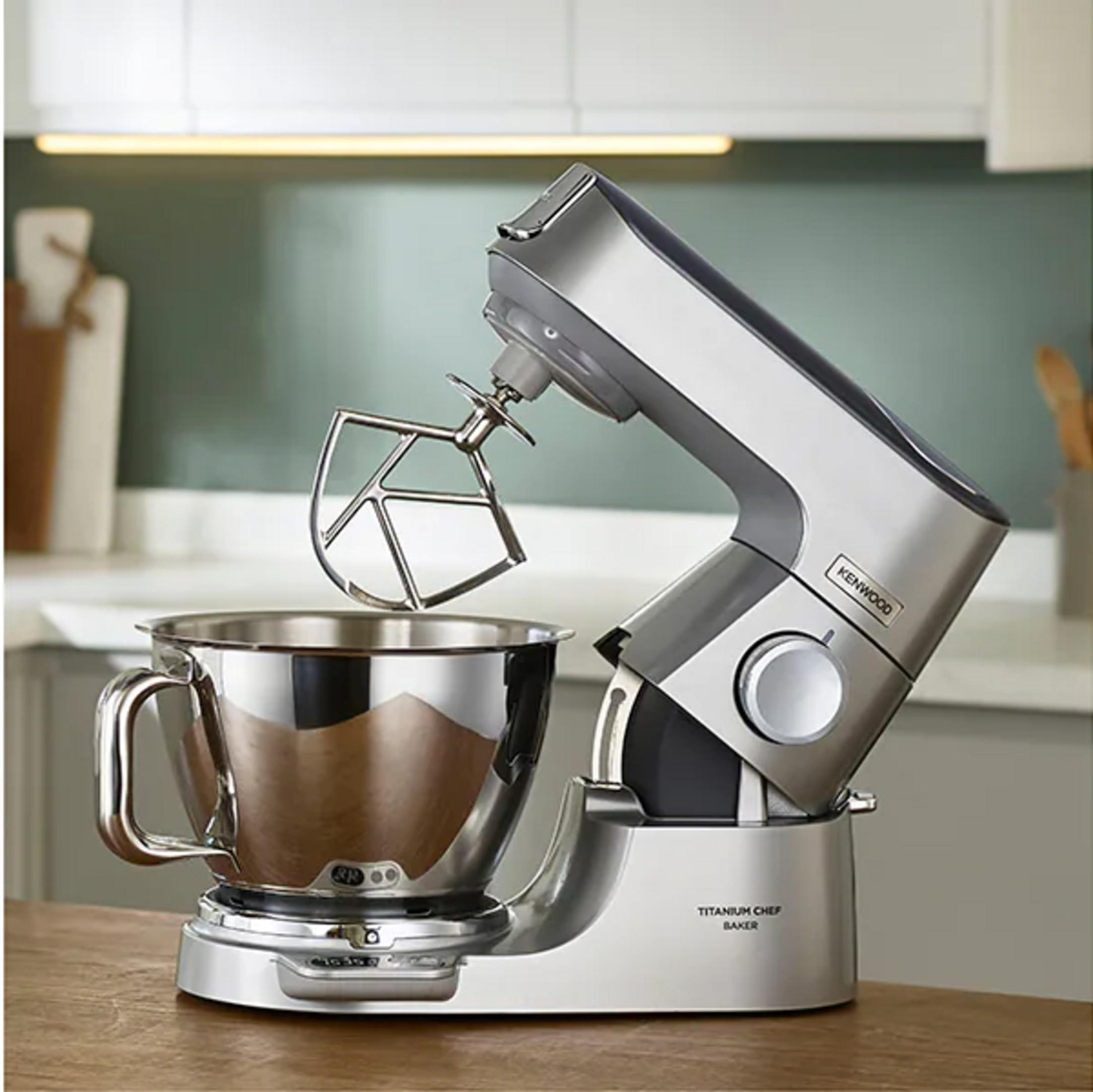 Un robot da cucina Kenwood argentato con ciotola e frusta su bancone.