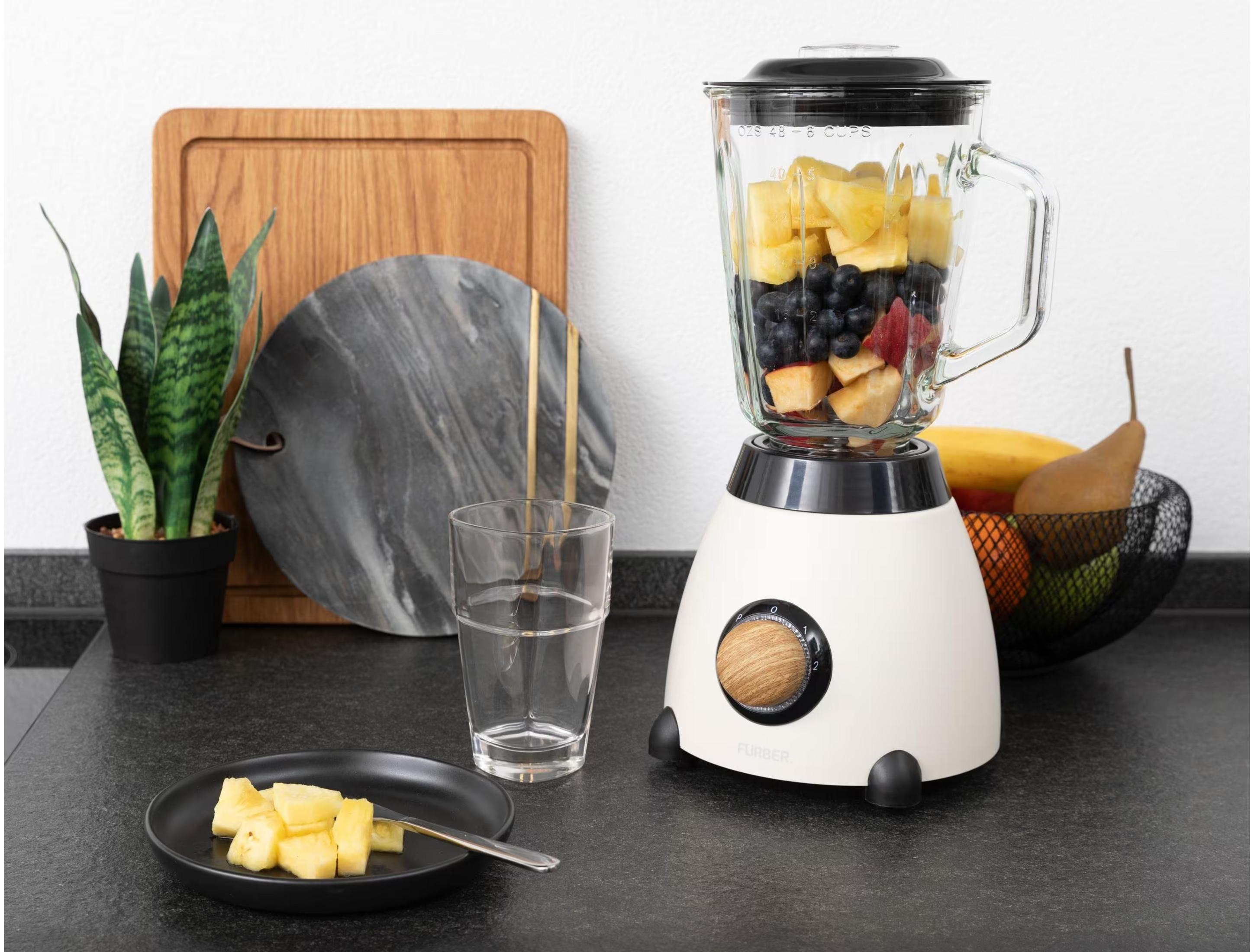 Un frullatore con frutta e un piatto di pezzi d'ananas su un piano di lavoro.