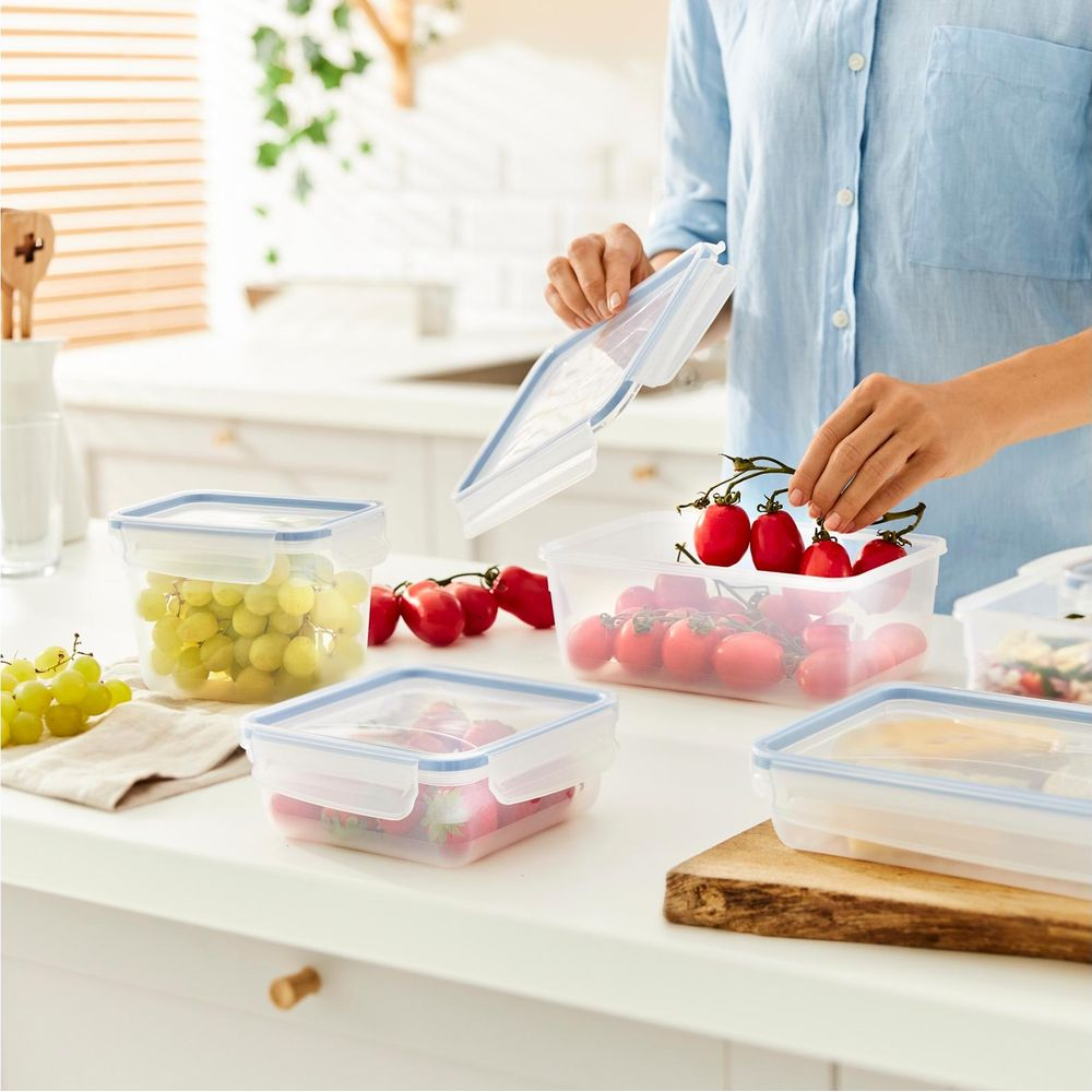 Persona che ripone uva, fragole e pomodori in contenitori trasparenti in una cucina.