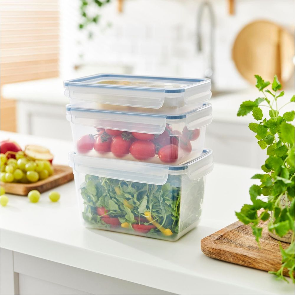 Tre contenitori per alimenti impilati: insalata, pomodorini e vuoto. Piano cucina.