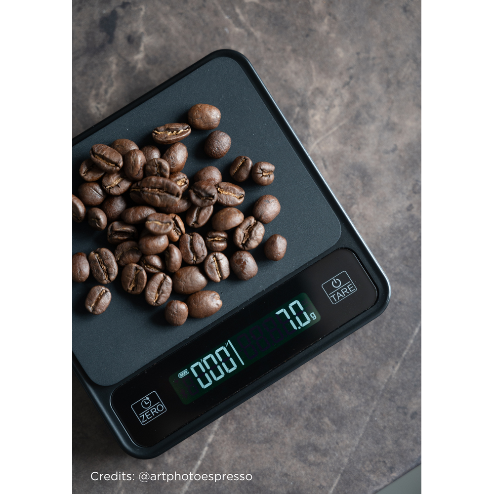 Une balance numérique avec des grains de café torréfiés. L'écran affiche 7,0 g.