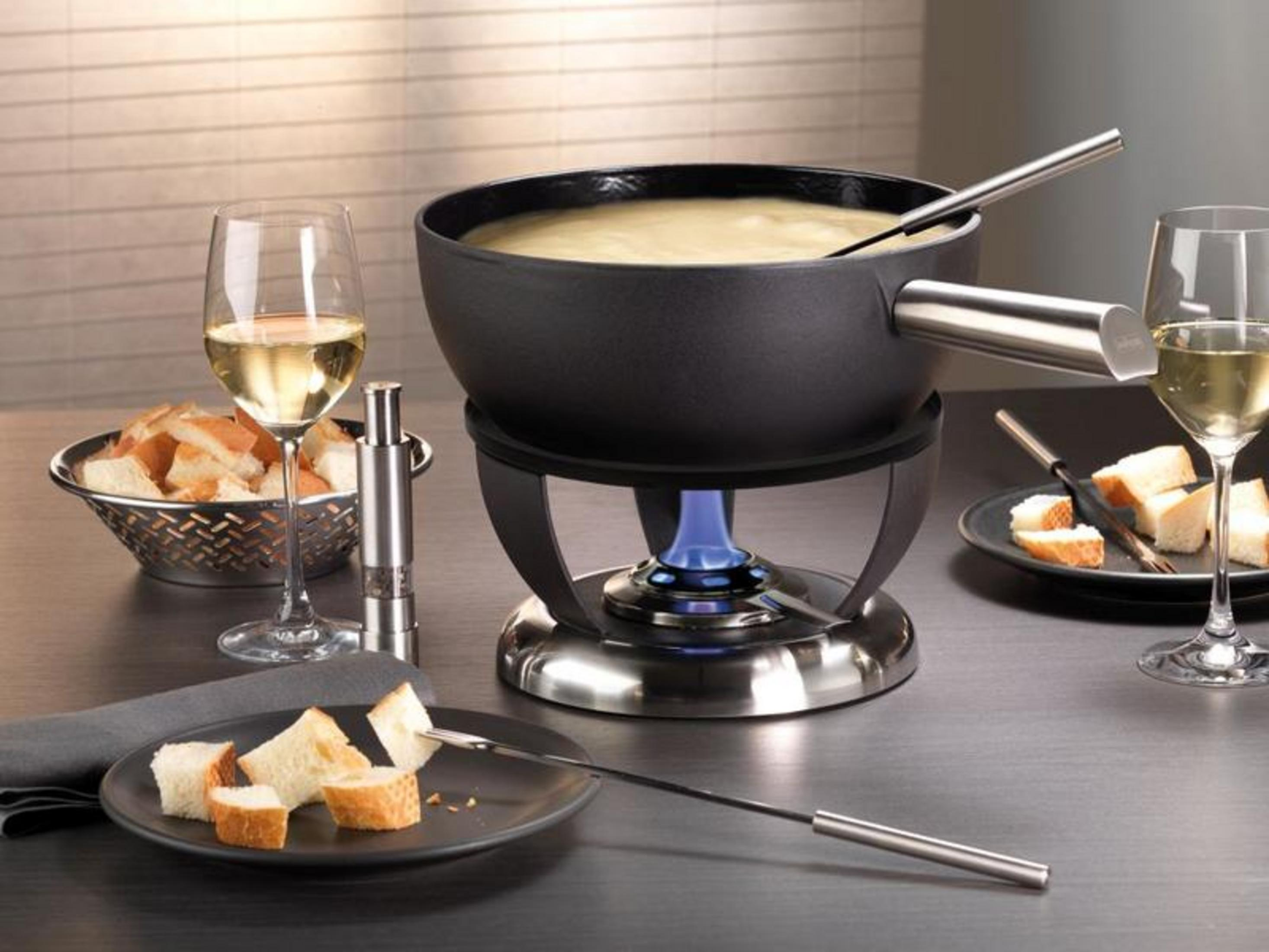 Ein Fondue-Set mit Brotstücken auf einem Tisch, daneben Wein.