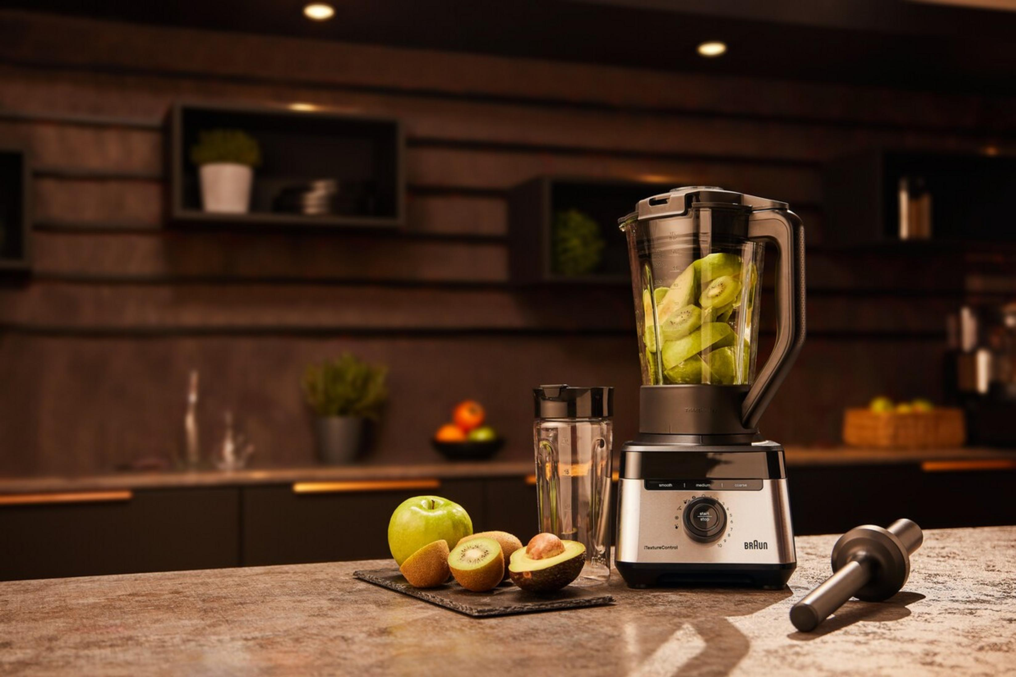 Ein Mixer mit Kiwistücken, daneben Obst und ein Stabmixer.