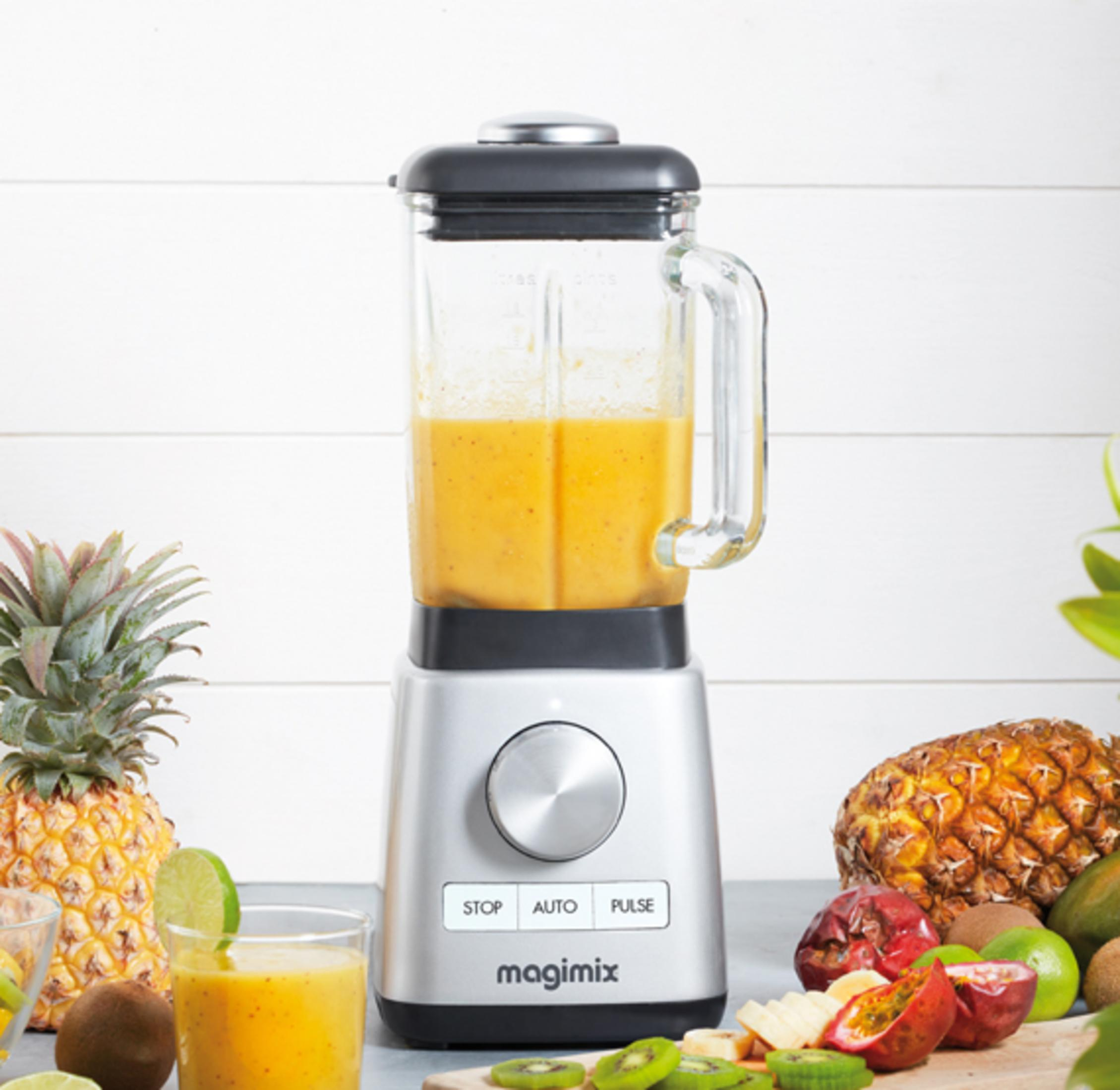 Ein silberner Mixer mit gelbem Smoothie und Früchten wie Ananas und Passionsfrucht.