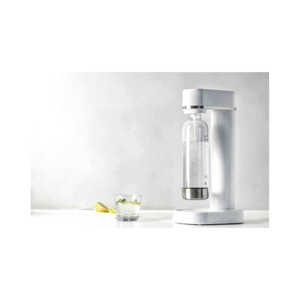 Un appareil à soda blanc avec une bouteille remplie et un verre de soda à côté.