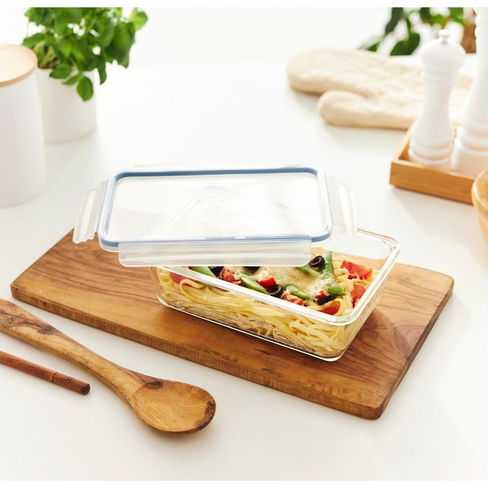 Contenitore in vetro con pasta, pomodori, olive e fagioli su tagliere in legno.