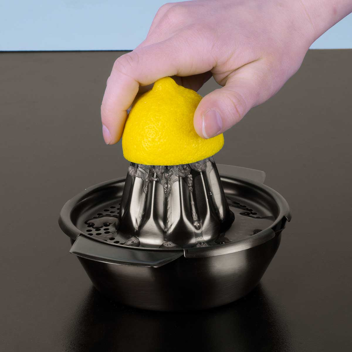 Una mano spremi un limone in uno spremiagrumi di metallo.