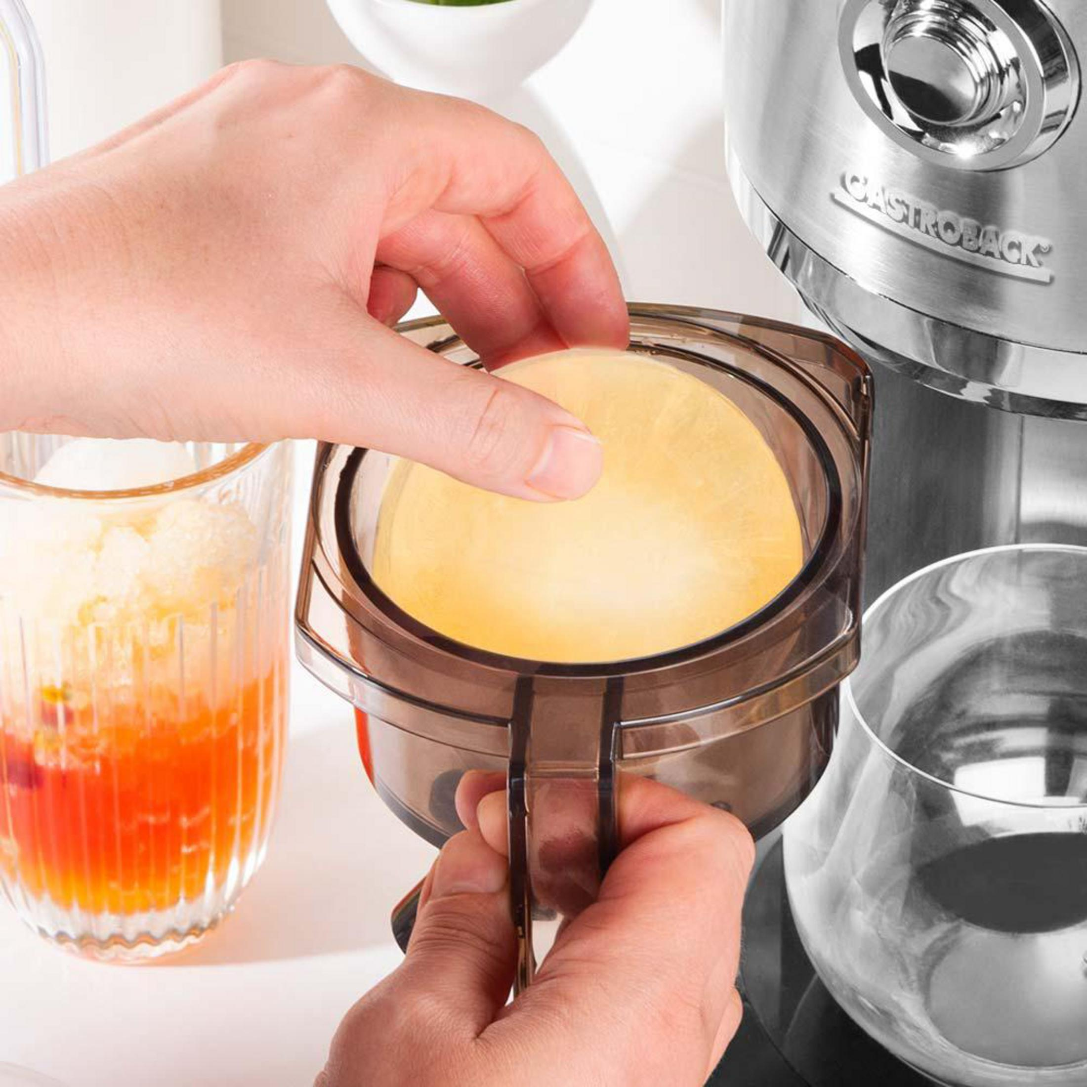 Le mani posizionano un filtro rotondo giallo in un contenitore trasparente accanto a un bicchiere di succo.