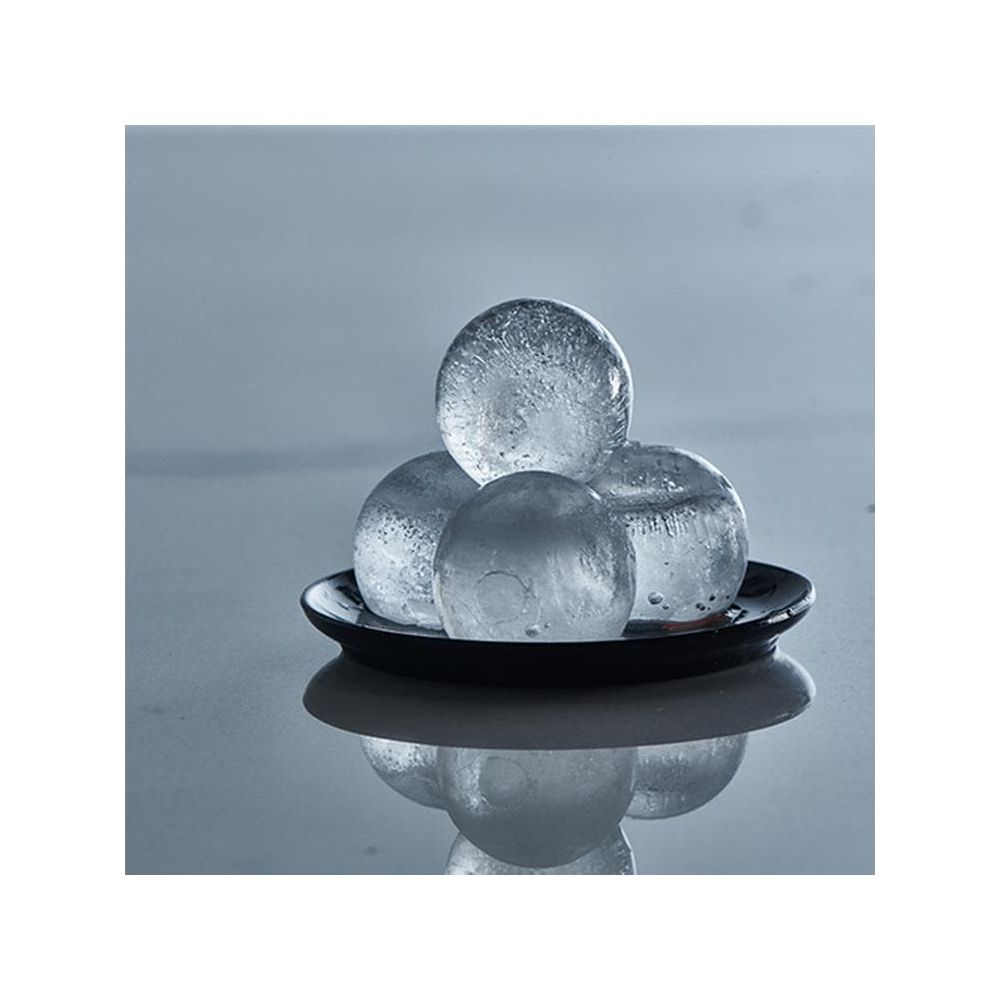 Quatre glaçons ronds empilés sur une assiette noire, avec reflet.