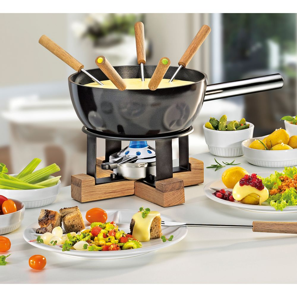 Ein Käsefondue-Set mit Brotstücken, Gemüse und Früchten auf einem Tisch.