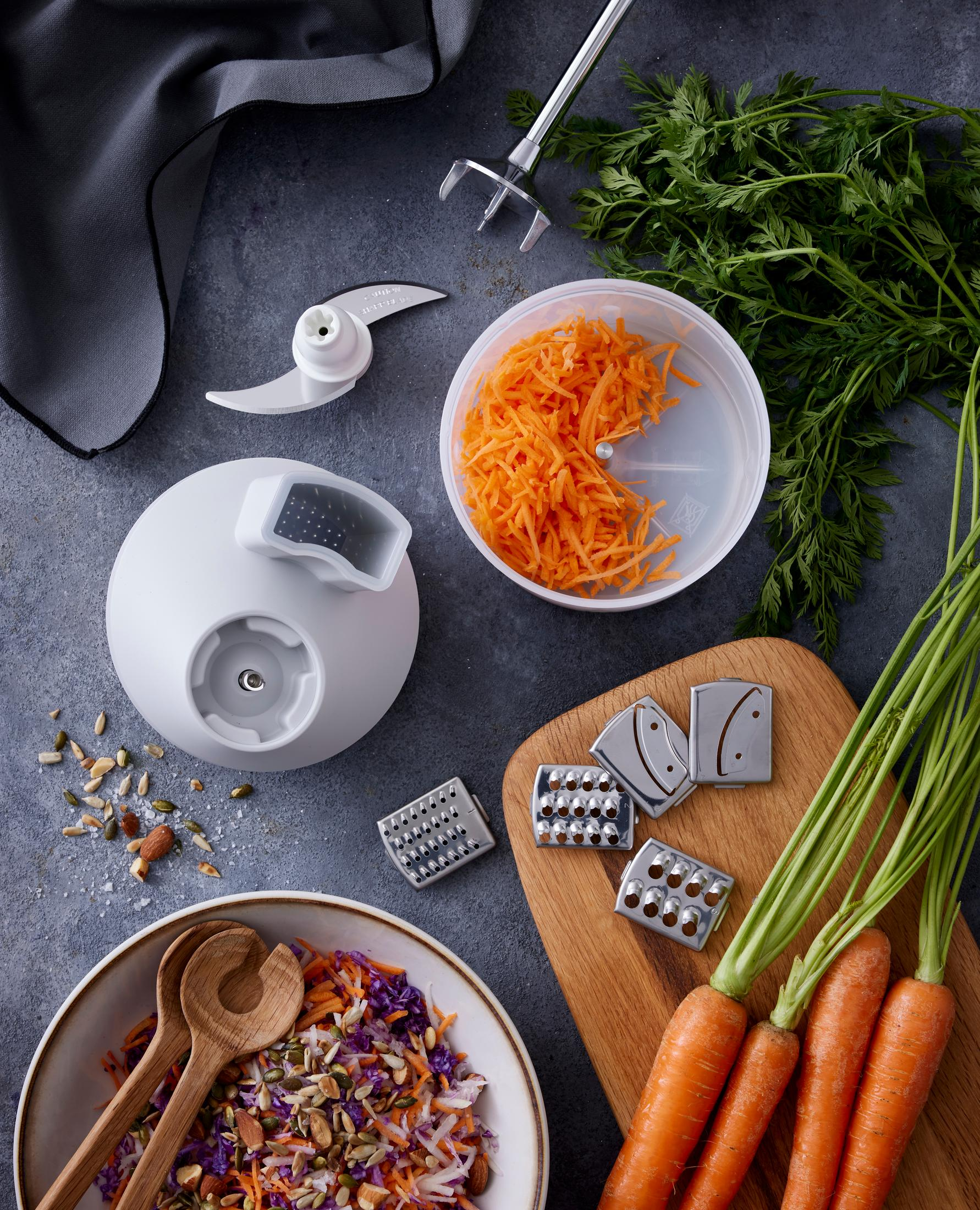 Robot culinaire avec carottes, râpes et salade dans un bol.