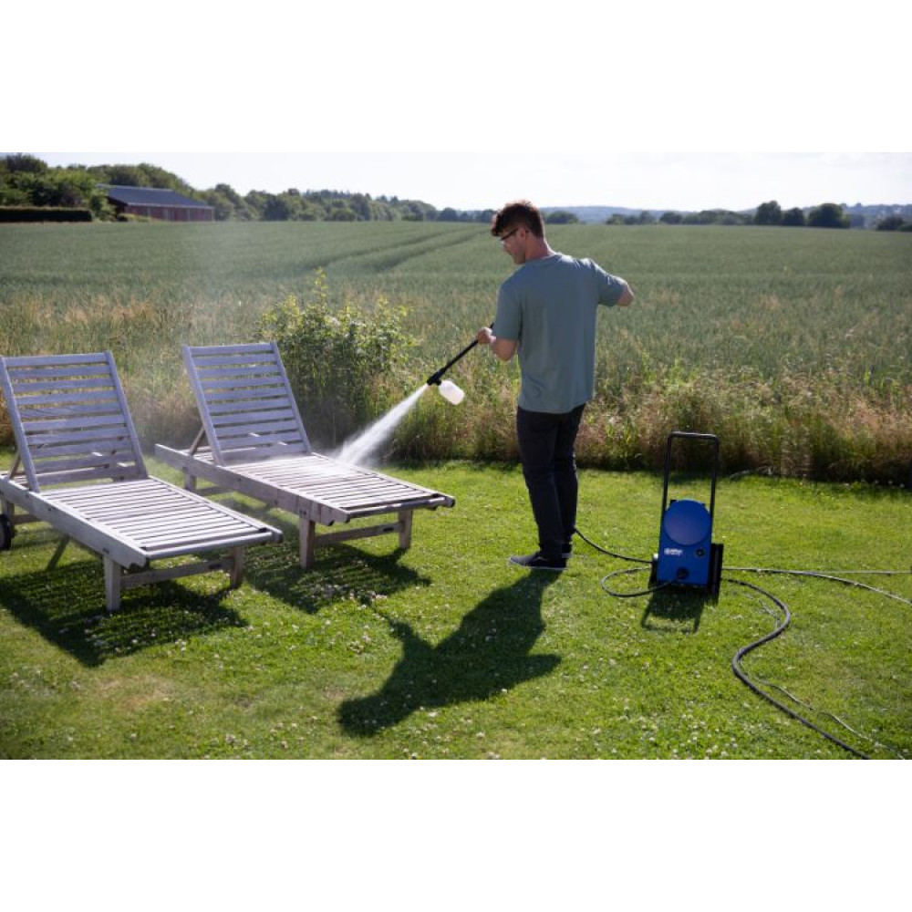 Mężczyzna myje ciśnieniowo drewniane leżaki na trawniku niebieską maszyną.