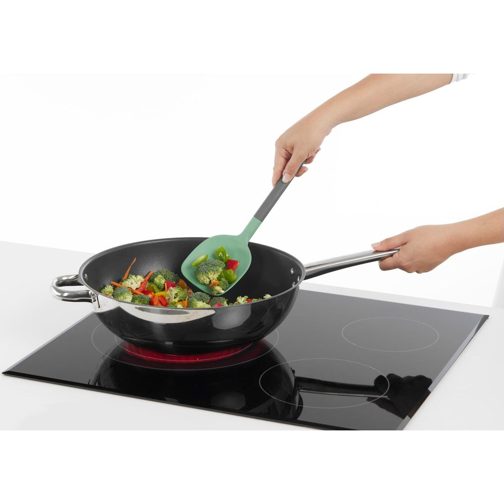 Des légumes sont remués dans un wok avec une spatule sur une plaque à induction.