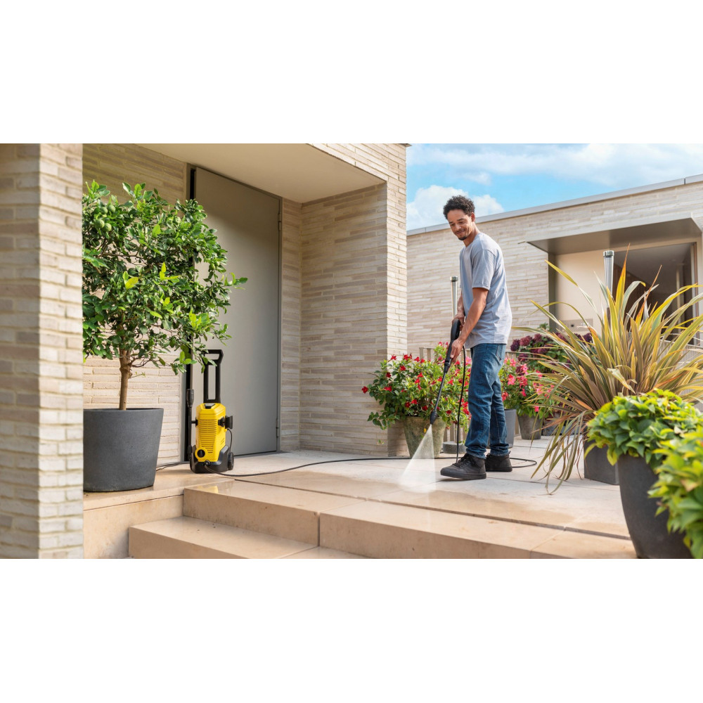 Mężczyzna czyści stopnie myjką ciśnieniową; żółta maszyna w pobliżu.