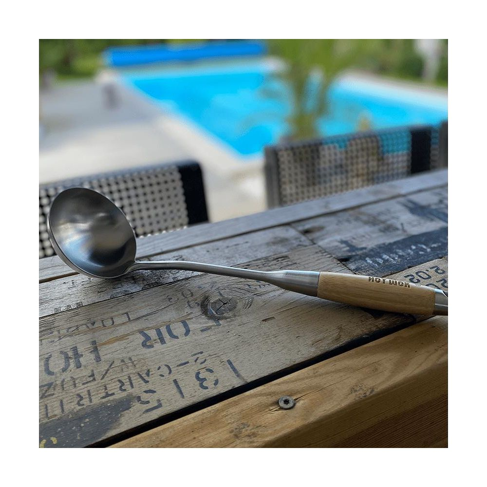 Metallschöpfkelle mit Holzgriff auf Holztisch vor Pool.