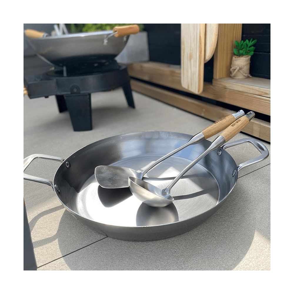 Ein großer, flacher Metalltopf mit zwei Kochutensilien mit Holzgriffen.