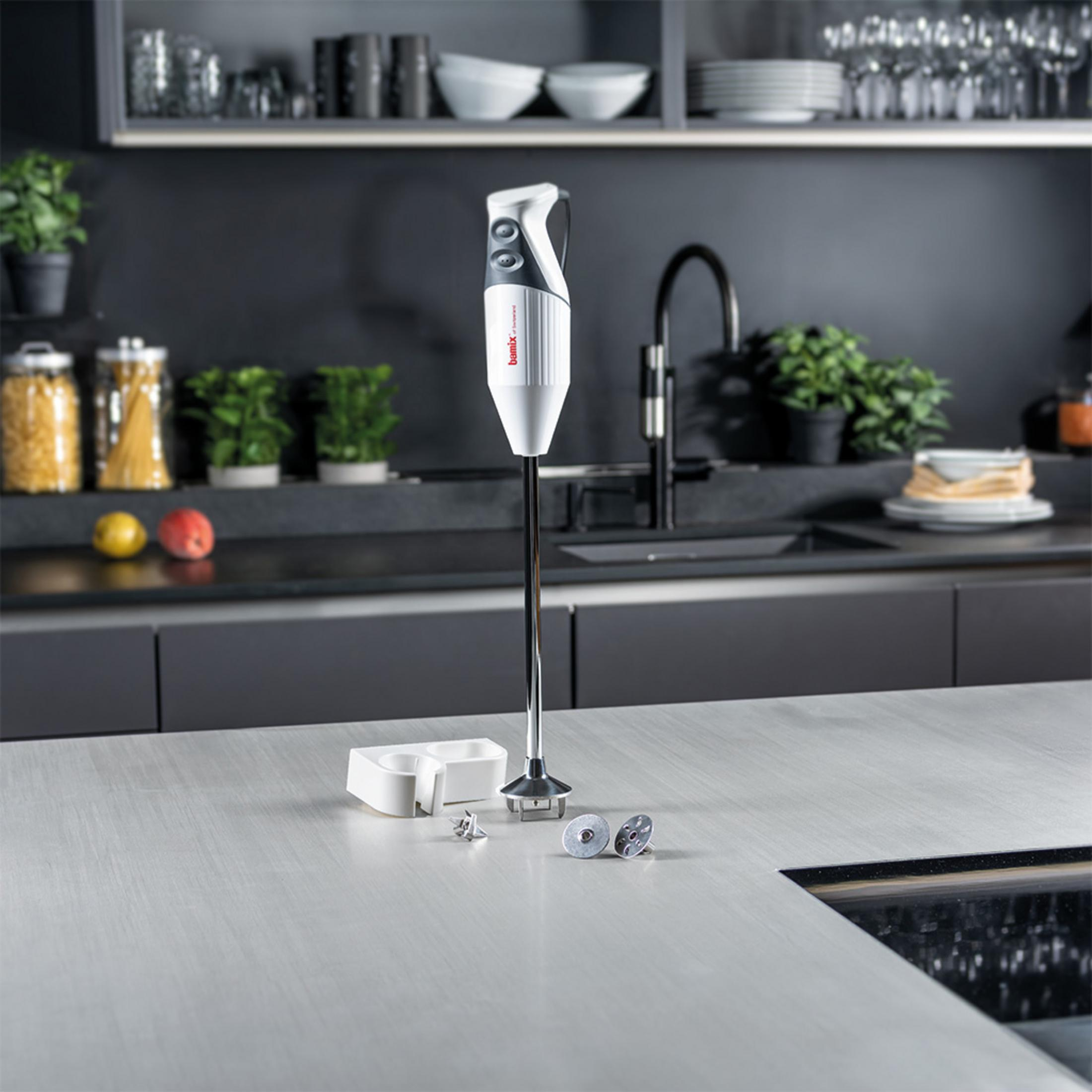Un mixeur plongeant blanc se dresse sur un comptoir de cuisine à côté d'accessoires.