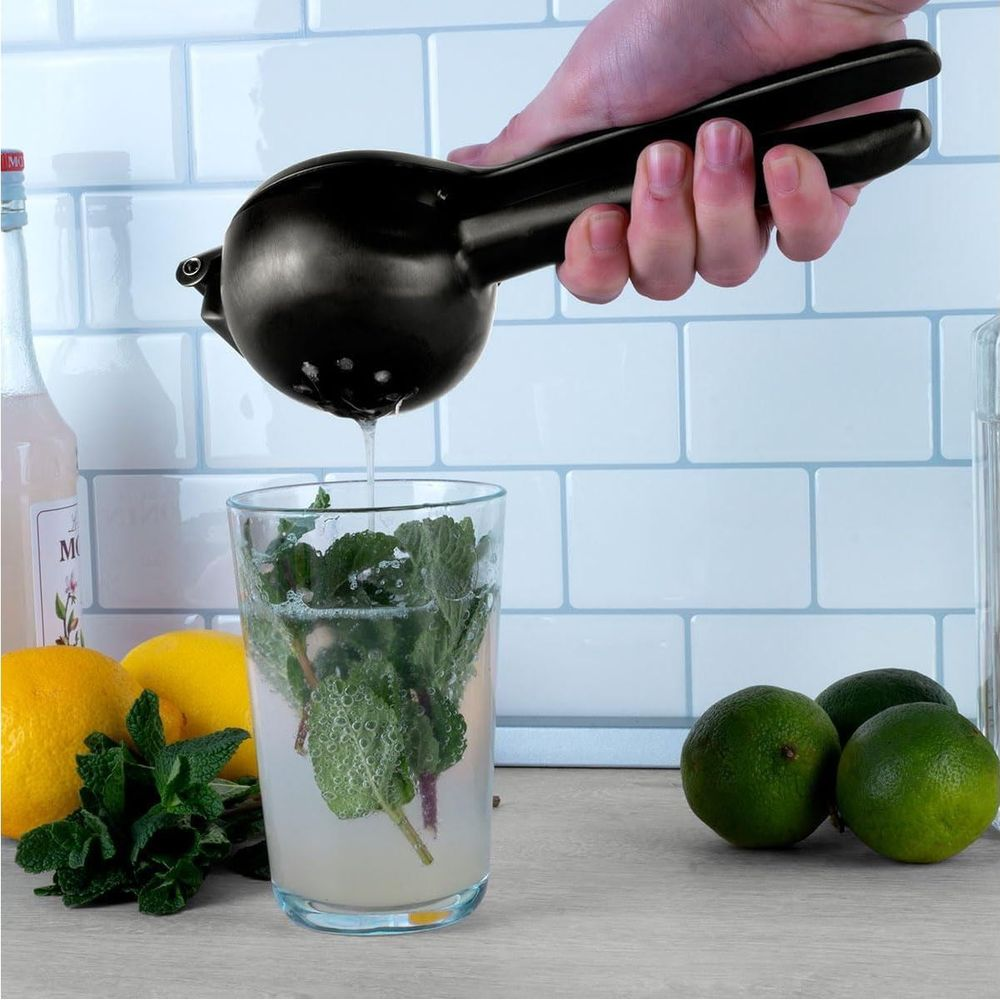 Una mano spremiagrumi nera preme su un bicchiere di menta e limonata.
