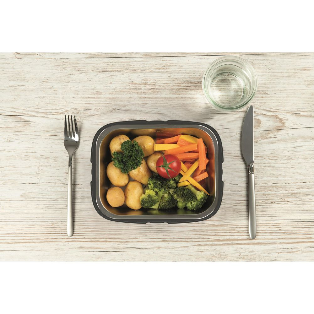 Ein Behälter mit Kartoffeln, Brokkoli, Karotten und Tomate, daneben Besteck und Glas.