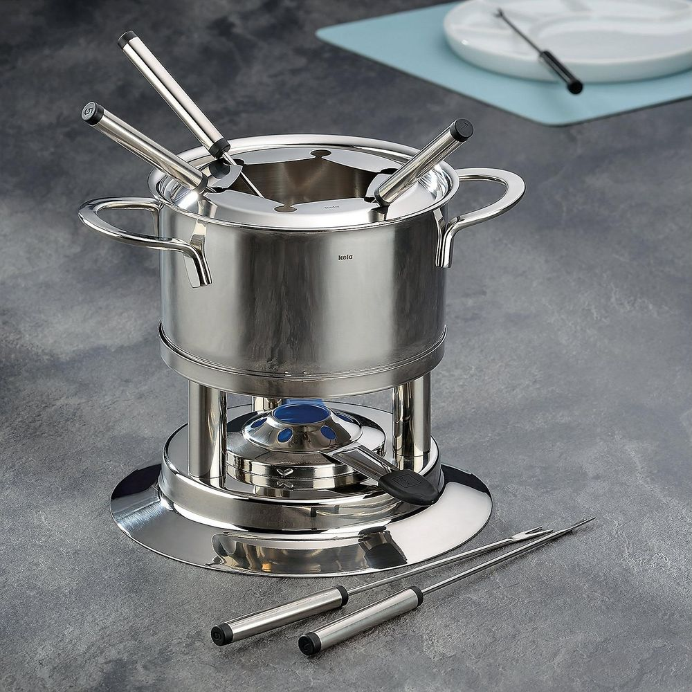 Un service à fondue argenté avec marmite, brûleur et fourchettes sur fond gris.