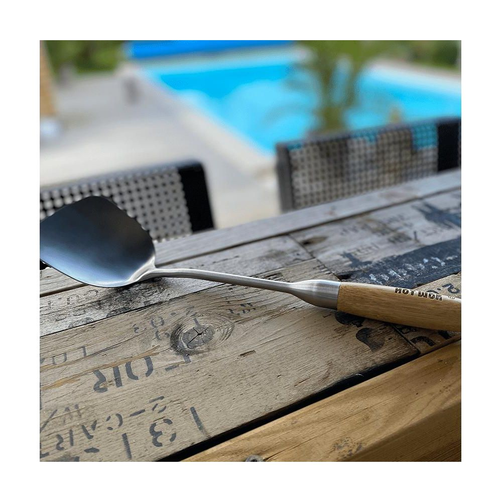 Une spatule à manche en bois repose sur une table en bois, avec une piscine en arrière-plan.