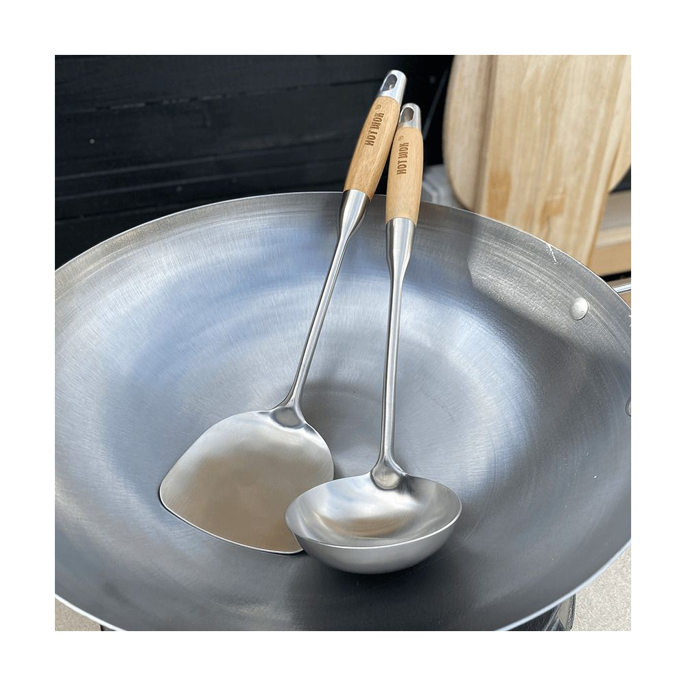 Un wok avec une spatule et une louche, toutes deux à manche en bois.