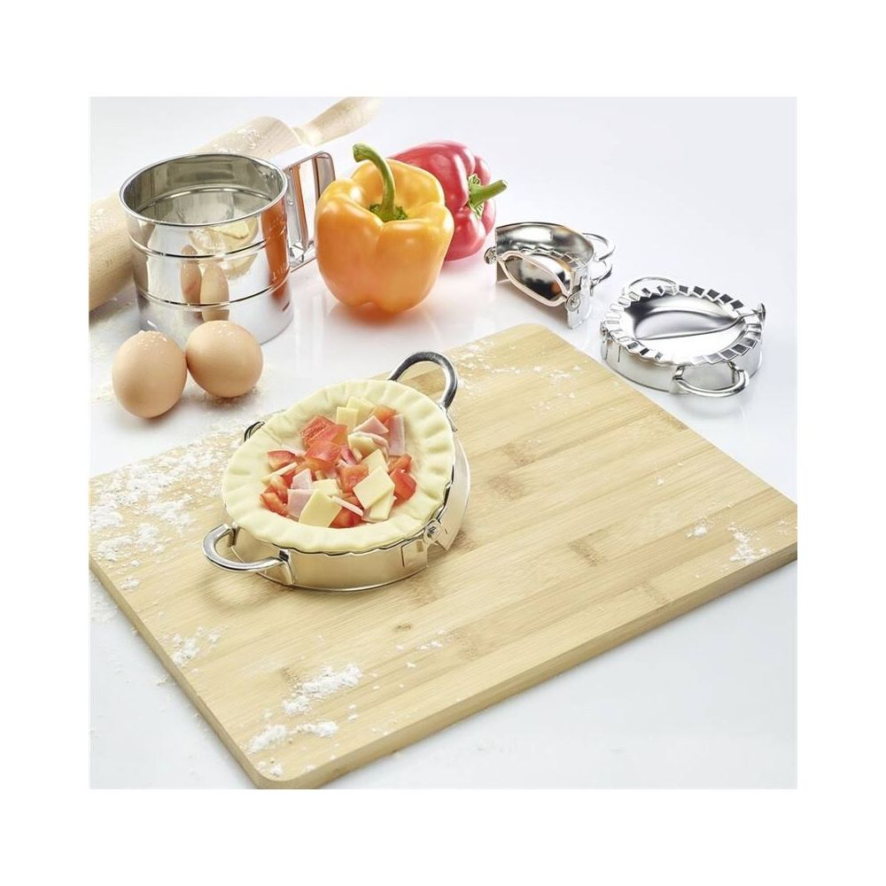 Un récipient à pâte avec garniture, œufs, poivrons, tamis à farine et emporte-pièces sur planche.