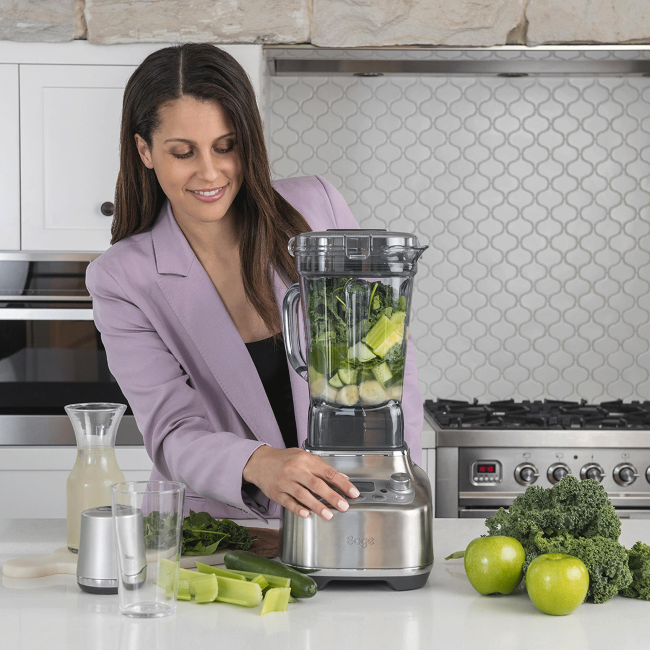 Une femme prépare un smoothie vert dans un mixeur dans une cuisine.