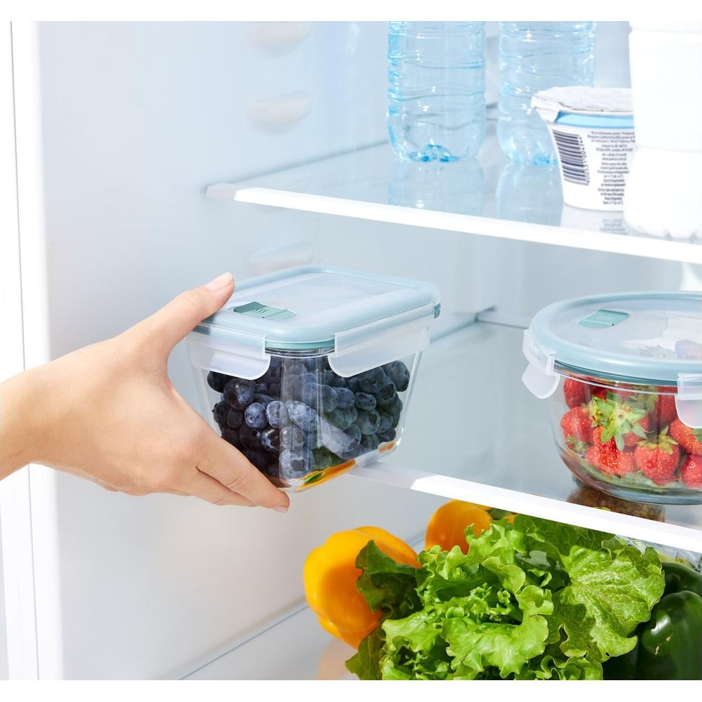 Mano mette contenitore con mirtilli in frigo accanto a fragole.