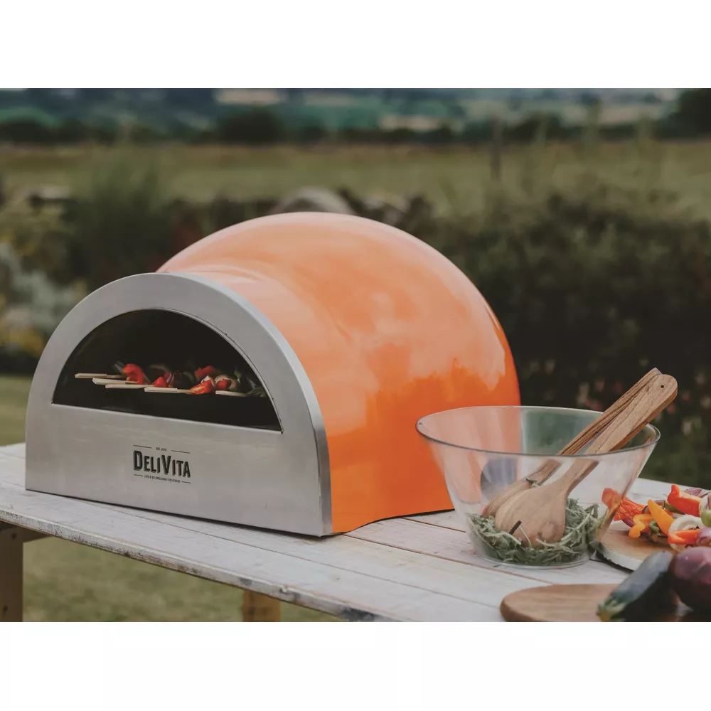 Un four orange avec brochettes et bol de salade sur table en bois.