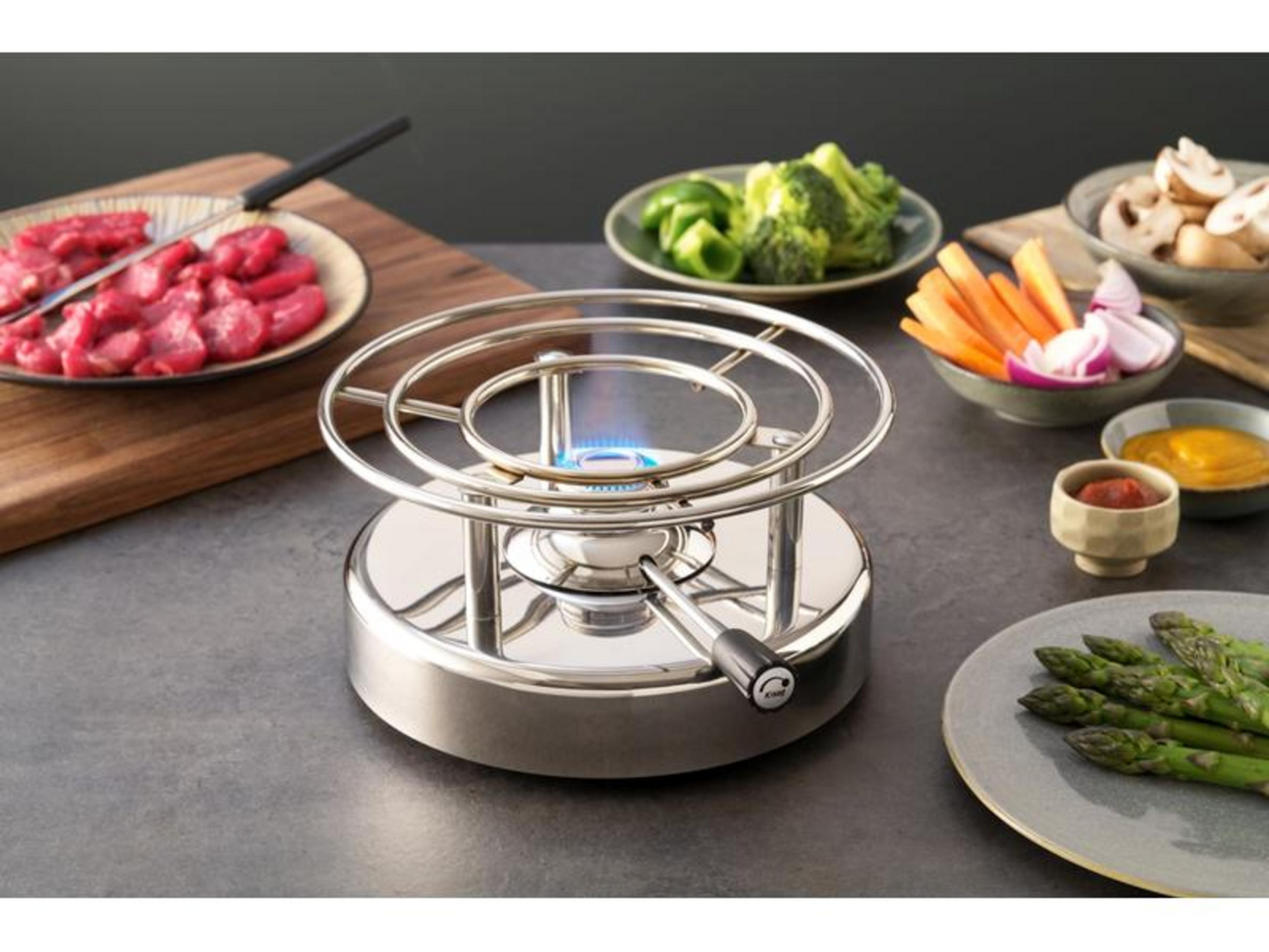 Ein Fondue-Set mit rohem Fleisch, Gemüse und einer brennenden Flamme.