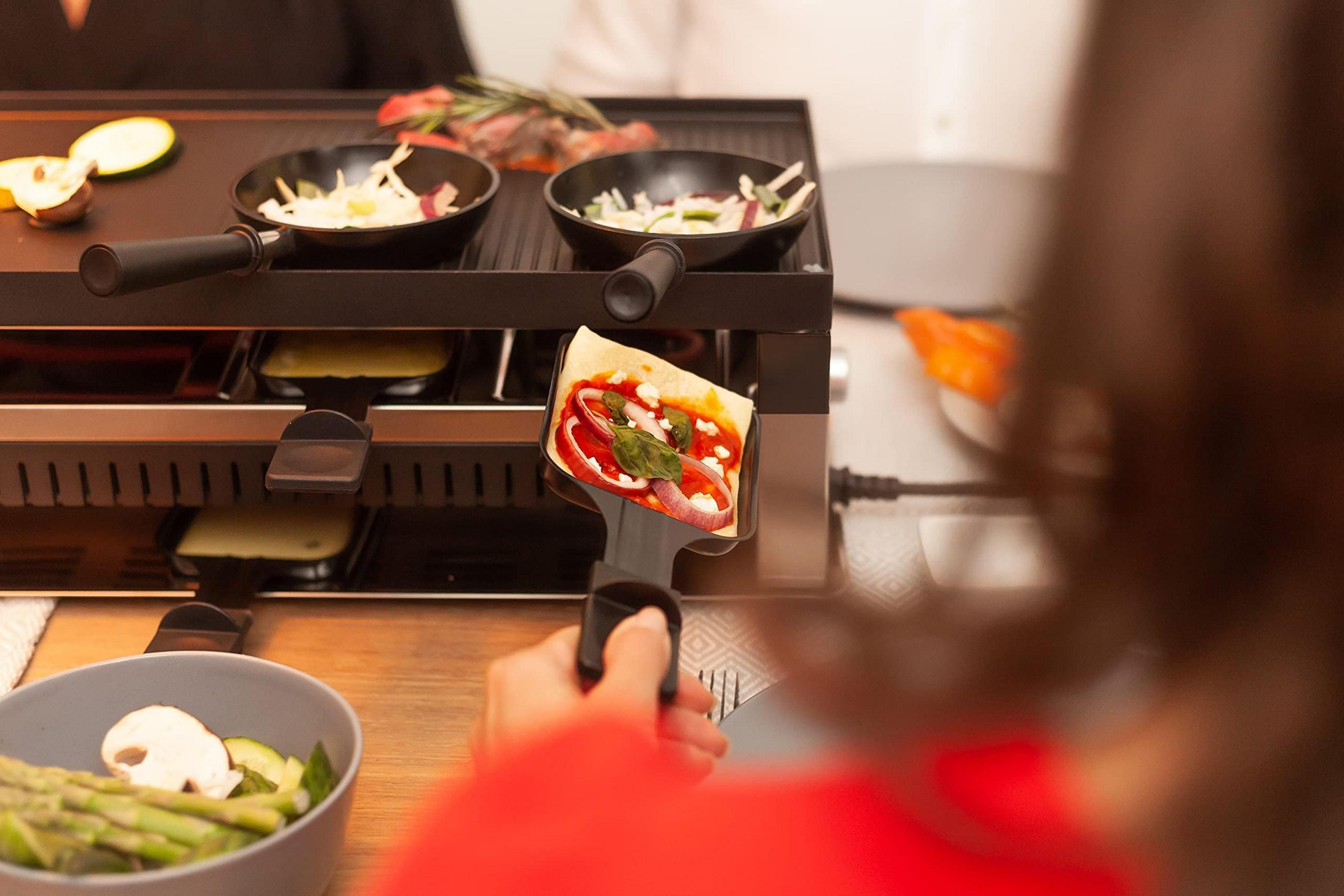 Una griglia per raclette con padelle e una pizza su una spatola.