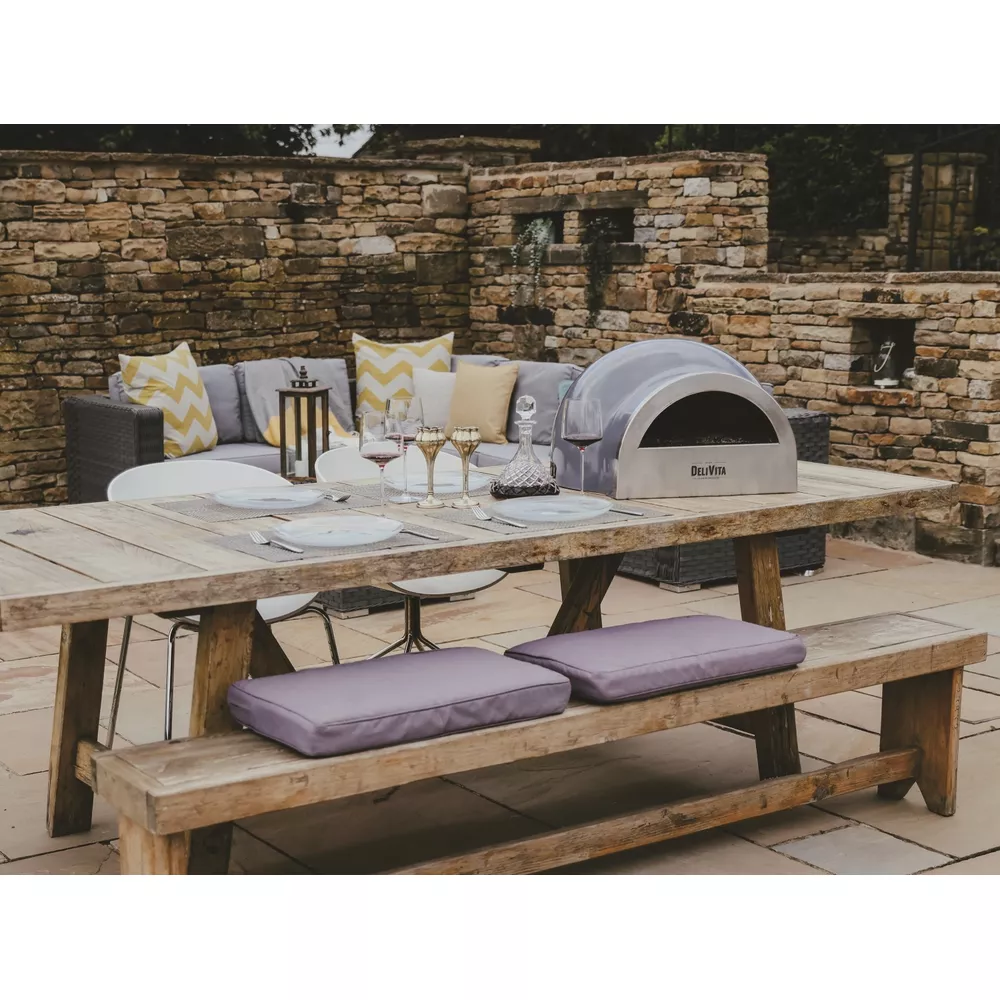 Une table en bois d'extérieur dressée pour dîner avec un four à pizza.