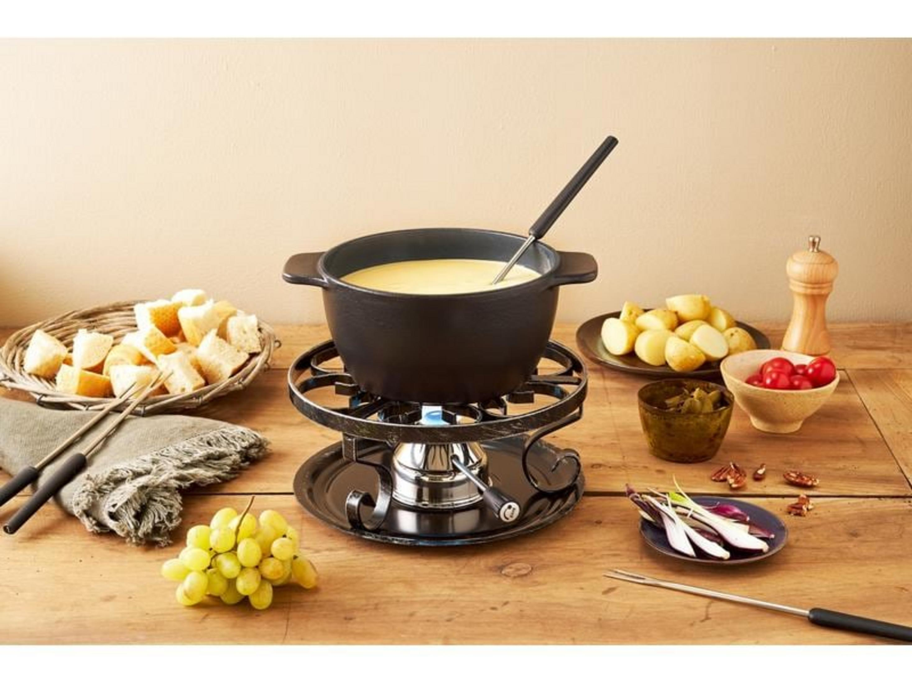 Käsefondue-Set mit Brot, Kartoffeln, Trauben und Gewürzen auf Holztisch.