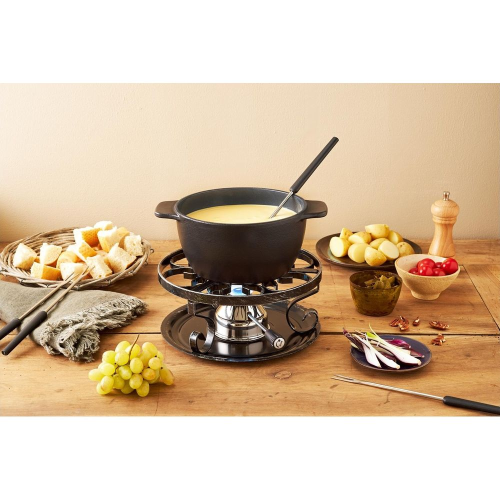 Ein Käsefondue-Set auf einem Holztisch mit Brot, Kartoffeln, Trauben und Kirschtomaten.