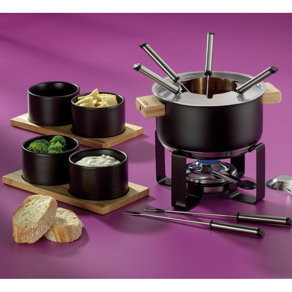 Un set da fonduta con ciotole nere di cibo su assi di legno, con una pentola da fonduta su un bruciatore.