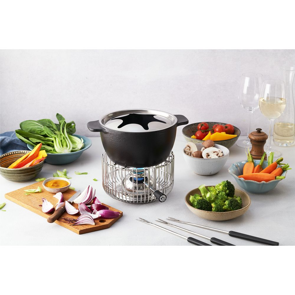 Ein Fondue-Set mit Gemüse, Gewürzen und Weingläsern auf einem Tisch.