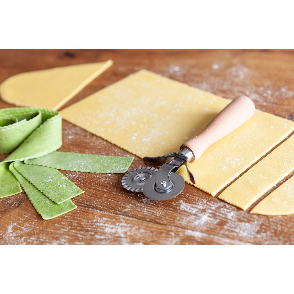 Un coupe-pâtes avec manche en bois repose sur de la pâte à pâtes jaune et verte.