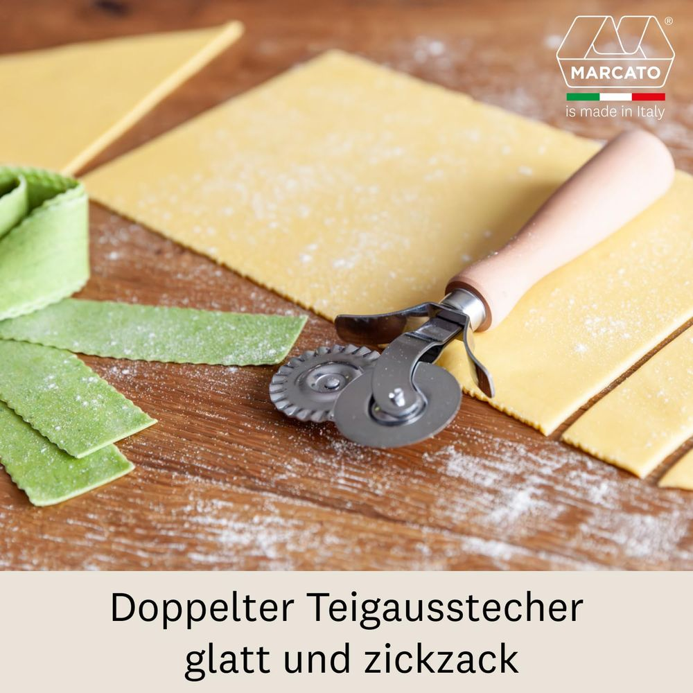 Une roulette à pâtes repose sur des feuilles de pâte jaune et verte sur une table en bois.
