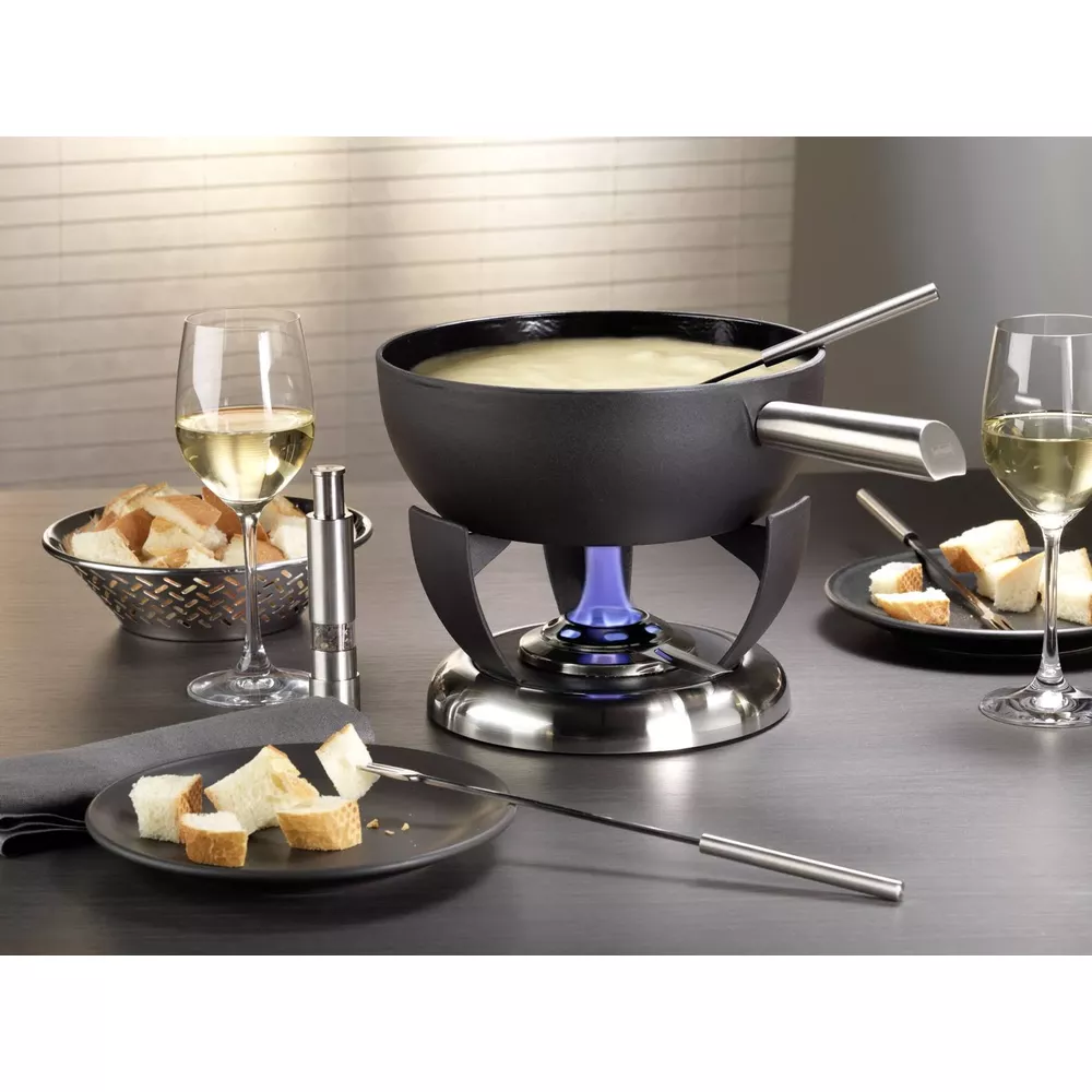 Käsefondue mit Brotstücken, Weißwein und Gewürzstreuer auf einem Tisch.